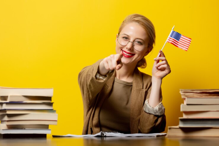 Foto estilo mulher loira sentada à mesa com livros e segura a bandeira dos eua em amarelo