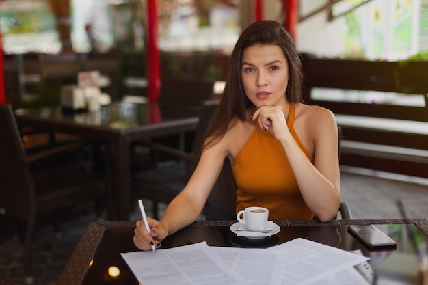 Foto estilo de negocios, chica con documentos y un bolígrafo con una taza de café en una cafetería en la calle