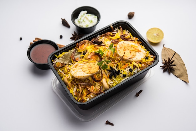 Estilo restaurante egg biryani ou anda pulao embalado para entrega ao domicílio em caixa de plástico ou recipiente com raita e salan