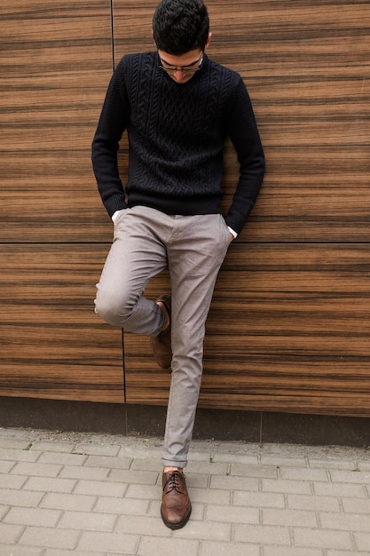 estilo de ropa casual cómoda de moda de negocios. hombre confiado relajado apoyado en la pared de textura de madera al aire libre