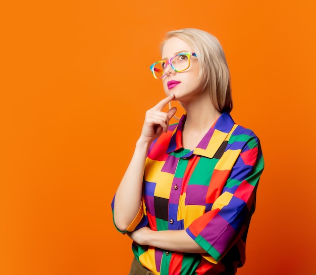 Estilo rubia con ropa de los 90 y gafas de arcoiris en naranja