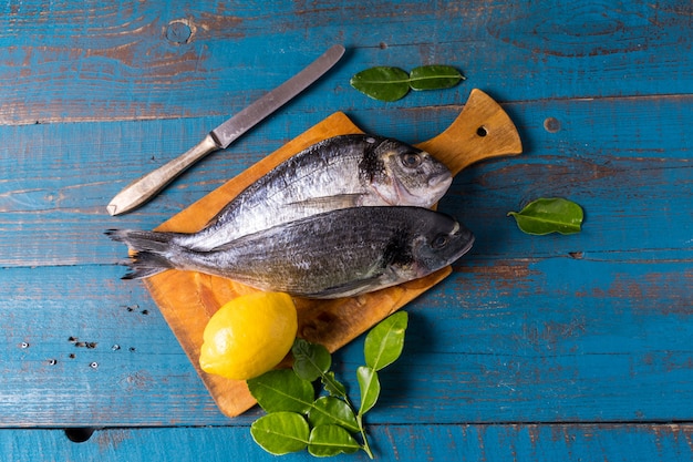 Estilo rústico. Pescado de lubina en un viejo fondo de madera azul, limón y cuchillo de cocina, antes de cocinar