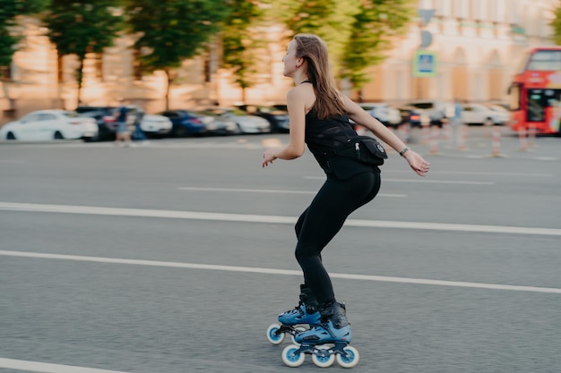 Estilo de vida activo y concepto de afición Una joven deportiva hace deporte al aire libre monta en patines vestida con ropa deportiva disfruta de poses de actividades físicas en un lugar urbano en la carretera Patinaje sobre ruedas