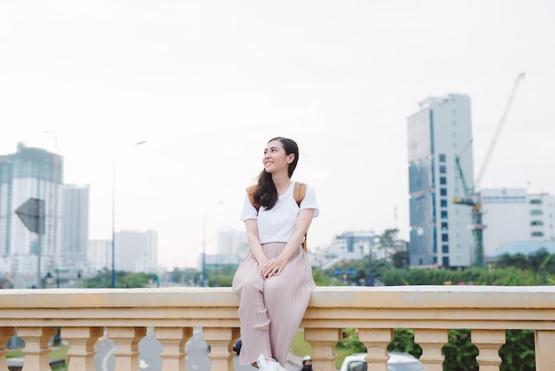 Estilo de vida al aire libre cerca retrato de mujer joven feliz en elegante traje casual sentado en el puente en la calle. Chica bonita hipster divirtiéndose y disfrutando de las vacaciones.