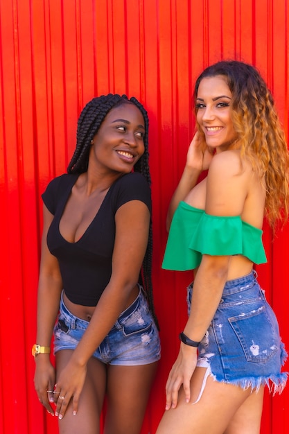 Estilo de vida de amigos chica rubia caucásica y chica negra con gran trenza en una pared roja