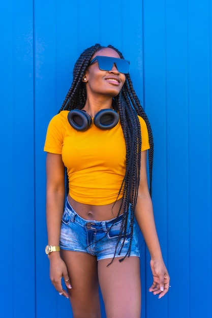 Estilo de vida, chica negra con largas trenzas, camiseta amarilla y gafas de sol. Chica sexy y dj con auriculares sonriendo