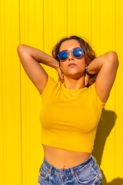 Estilo de vida, chica rubia caucásica con camisas amarillas en una pared amarilla. Chica guapa de moda posando en una expresión tranquila, con gafas de sol