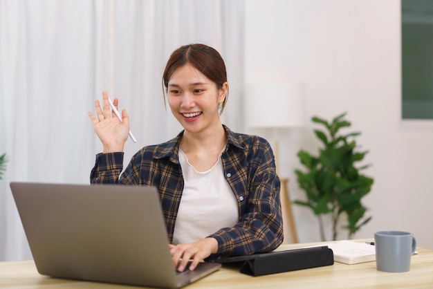 Estilo de vida en concepto de sala de estar Mujer asiática hace gesto de saludo con colega en videollamada