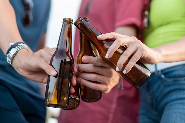 Estilo de vida COVID con gente brindando con cerveza embotellada. Personas borrosas con mascarilla. Centrarse en las botellas.