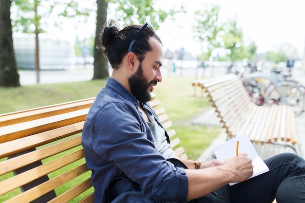 estilo de vida, creatividad, freelance, inspiración y concepto de personas - hombre creativo con cuaderno o escritura de diario sentado en el banco de la calle de la ciudad