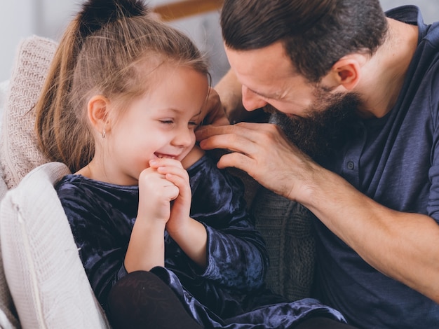 Estilo de vida de crianza feliz. Padre cariñoso que complementa a su linda hijita, niña tímida, sonriendo.