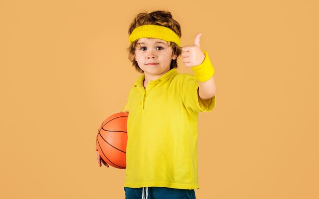 Foto estilo de vida deportivo activo juego de baloncesto niño pequeño deportivo con pelota de baloncesto mostrando el pulgar hacia arriba niño