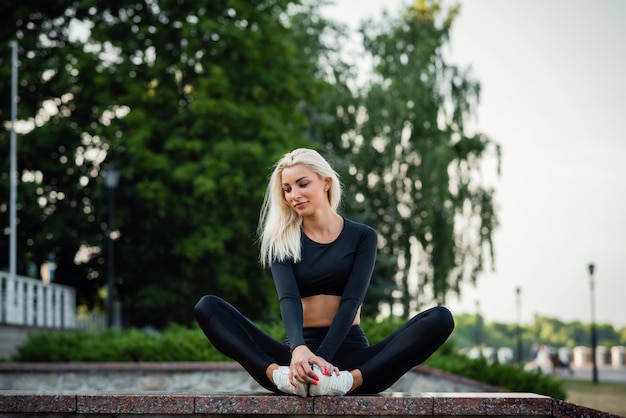 Estilo de vida deportivo saludable. La mujer hermosa joven en una ropa de deportes se sienta en parque de la ciudad