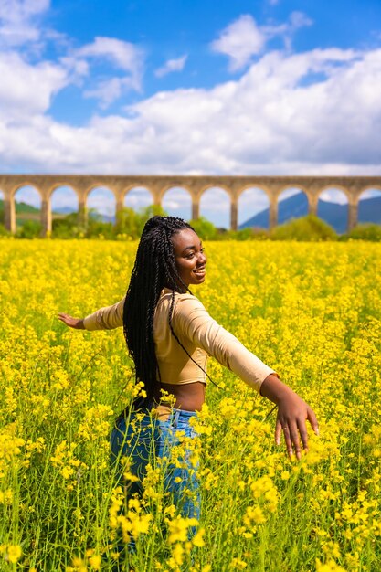 Estilo de vida disfrutando de la naturaleza en libertad retrato de una chica étnica negra con trenzas viajera en un campo de flores amarillas