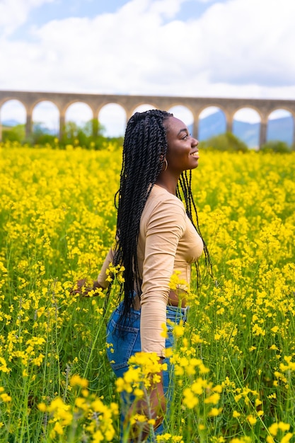 Estilo de vida disfrutando de la naturaleza retrato sonriente de niña étnica negra con trenzas viajero en un campo de flores amarillas