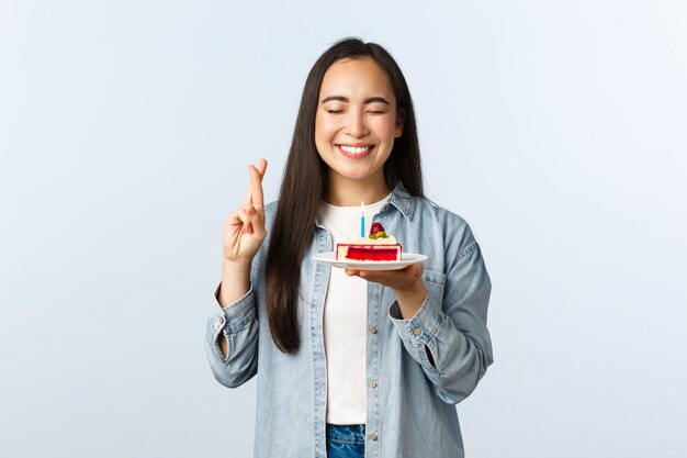 Estilo de vida de distanciamiento social, pandemia de covid-19, celebrando las vacaciones durante el concepto de coronavirus. Esperanza feliz asiática bithday girl cierra los ojos y sonríe mientras pide un deseo sobre el pastel de cumpleaños.