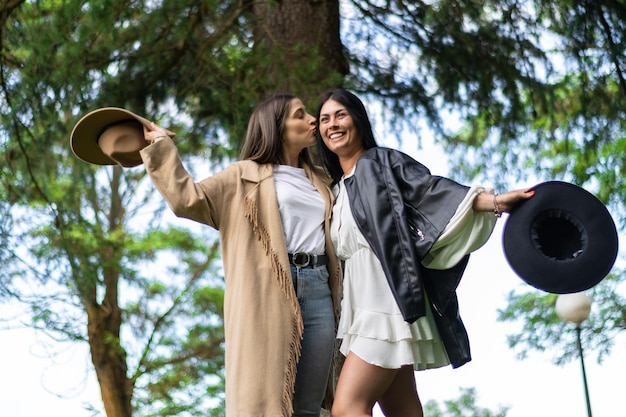 Estilo de vida de dos chicas con sombreros besándose en la mejilla en la hierba Dos felices mejores amigas con sombreros besándose las mejillas al aire libre Concepto de amistad de chicas