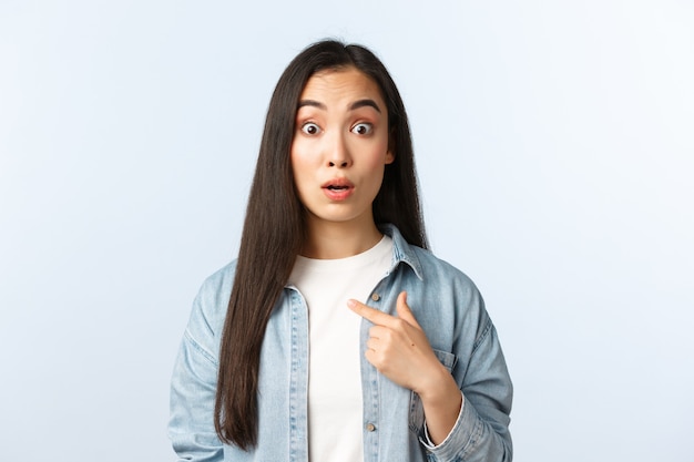 Estilo de vida, emociones de las personas y concepto de belleza. Chica asiática sorprendida y confundida apuntando a sí misma con los ojos muy abiertos y las cejas levantadas, siendo elegida o nombrada, fondo blanco.