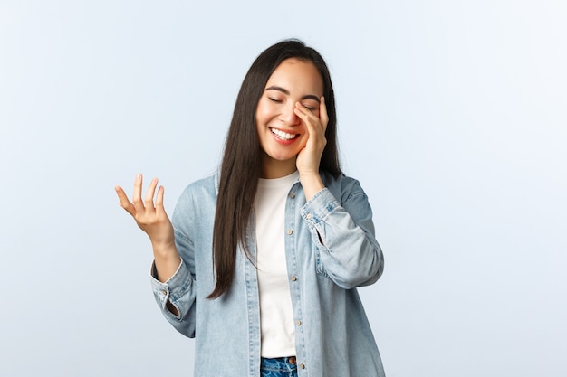 Estilo de vida, emociones de las personas y concepto de belleza. Despreocupada joven adolescente asiática moderna en ropa casual, riendo con los ojos cerrados, mirada conmovida, hablando, teniendo una conversación amistosa.