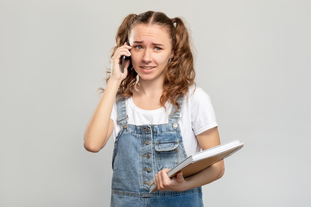 Estilo de vida del estudiante Llamada telefónica Chica confundida con el libro usando el móvil aislado en el fondo del espacio de copia neutral Comunicación a distancia