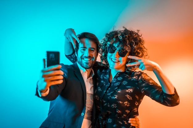 Estilo de vida de fiesta una pareja caucásica enamorada tomándose un selfie en una fiesta con luces naranjas y azules en el Día de San Valentín