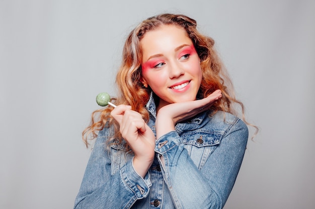 Estilo de vida, gente, concepto creativo - retrato de primer plano de retrato de mujer morena con labios rojos. Hermosa joven sostiene en manos dulces sonriendo ampliamente. Dulces y maquillaje brillante chica elegante