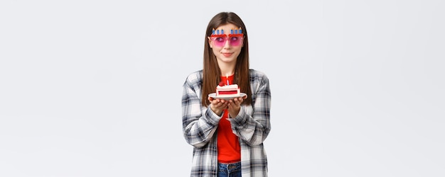 Estilo de vida de la gente vacaciones y concepto de emociones de celebración Linda y tonta cumpleañera con gafas divertidas mira hacia otro lado piensa en el deseo como una vela encendida en el pastel de cumpleaños sonriendo emocionada