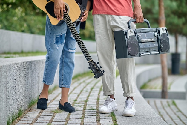 Estilo de vida. Guitarra y grabadora en manos de un joven de piel oscura y una chica parados en el parque, sin rostro