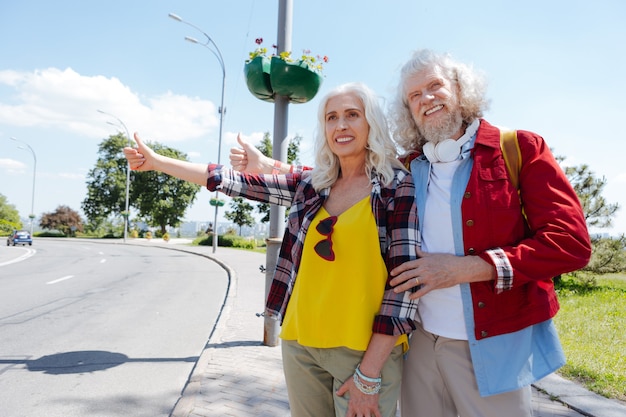 Estilo de vida hippy. Pareja de hippy envejecido de pie al lado de la carretera mientras pide un paseo