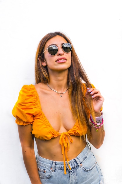 Estilo de vida de una joven morena caucásica con camiseta naranja, gafas de sol y pantalón corto sobre un fondo blanco, con espacio de copia y palos. Con una mirada dulce y seductora