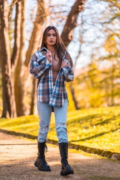 Estilo de vida, joven morena caucásica con un suéter de lana a cuadros y jeans rotos caminando en un parque en otoño