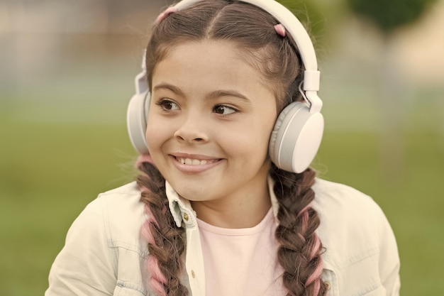 Estilo de vida moderno Los niños pequeños disfrutan escuchando música moderna al aire libre Niña con auriculares estéreo modernos en verano Usando tecnología moderna para el placer y la educación