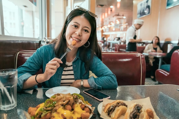 Estilo de vida de mujer local asiática en EE. UU. Comiendo comida rápida y bebiendo bebidas en el restaurante American Diner. joven turista usa tenedor almorzando cara cámara sonriendo atractivo. orden de cliente de camarero