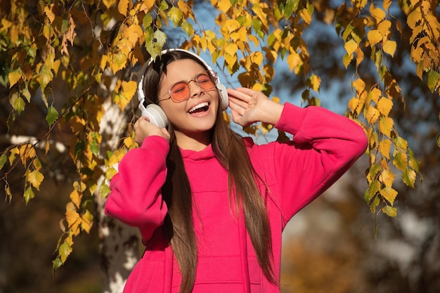 Estilo de vida musical de una adolescente cantando y usando auriculares en otoño o otoño en el parque al aire libre