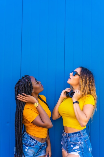 Estilo de vida, niña negra y rubia caucásica vestida de amarillo. Mirando hacia arriba, con auriculares y gafas de sol