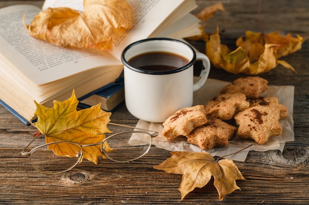 Estilo de vida otoñal: chocolate caliente, galletas con chispas de chocolate, libro antiguo, manta cálida, fondo de madera rústica,