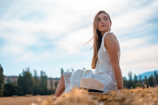 Estilo de vida rural, una joven campesina rubia sentada en un campo de paja