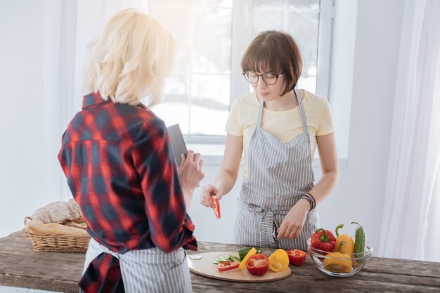 Estilo de vida saludable. Agradable agradable mujer inteligente de pie en la cocina y preparar una cena saludable mientras corta verduras