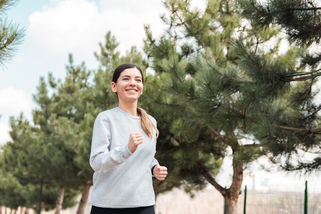 Estilo de vida saludable. alegre atractiva mujer corriendo en el parque con pinos en la mañana