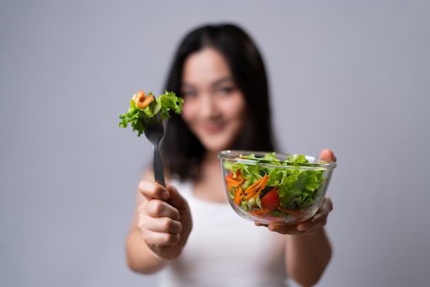 Estilo de vida saludable con concepto de comida limpia. Mujer asiática feliz comiendo ensalada aislada sobre la pared blanca.