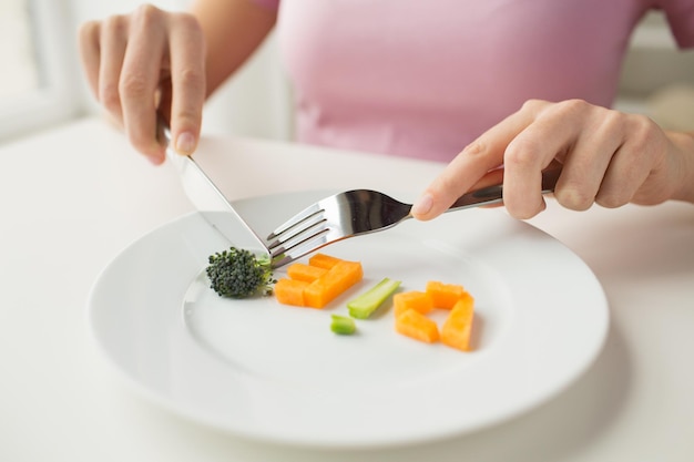 estilo de vida saludable, dieta, comida vegetariana y concepto de la gente - cierre de mujer con tenedor y cuchillo comiendo letras vegetales en el plato