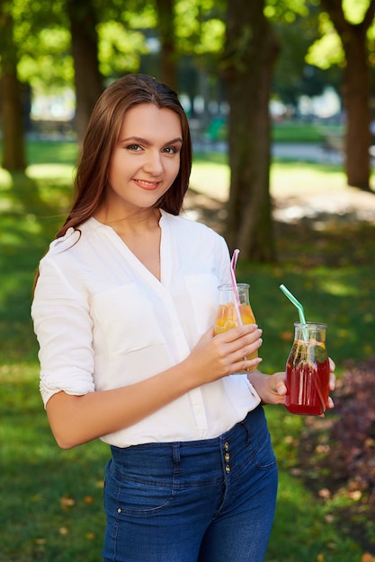 Estilo de vida saludable. Linda mujer joven con batido de desintoxicación de frutas en verano, sobre fondo verde de la naturaleza.