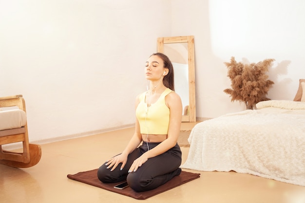 Un estilo de vida saludable. Una mujer hace ejercicio y escucha música. Sentado en una colchoneta de fitness. Yoga