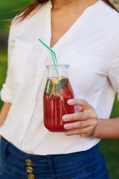 Estilo de vida saludable. Mujer joven irreconocible con batido de desintoxicación de bayas amarillas en verano, sobre fondo verde de la naturaleza.