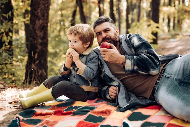 Estilo de vida saludable Picnic en la naturaleza Merienda saludable Carga de vitaminas Picnic familiar Hipster barbudo papá con hijo pasan tiempo en el bosque Brutal hombre barbudo y niño pequeño comen manzanas Bosque picnic senderismo