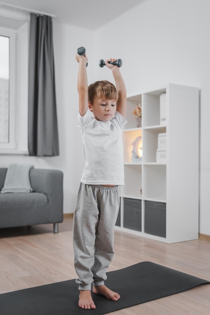 Estilo de vida saludable Retrato de un niño haciendo ejercicio con pesas en casa en la sala de estar