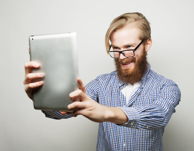 Estilo de vida, tecnología y concepto de personas: Selfie feliz. Joven barbudo sosteniendo una tableta y haciéndose una foto mientras está de pie contra el fondo blanco