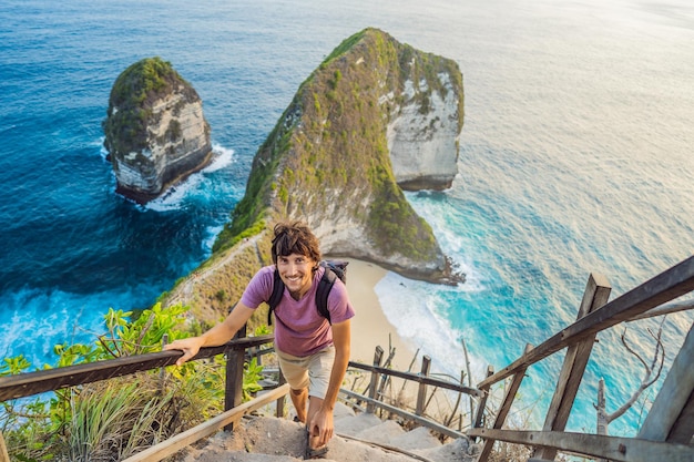 Estilo de vida de vacaciones familiares Hombre feliz parado en el mirador Mirar la hermosa playa bajo un alto acantilado Destino de viaje en Bali Lugar popular para visitar en la isla de Nusa Penida