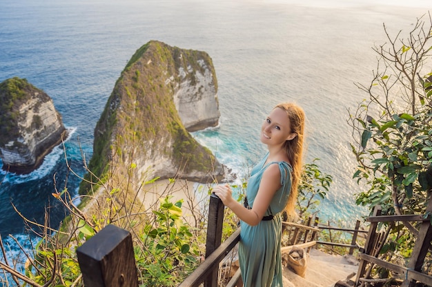 Estilo de vida de vacaciones familiares Mujer feliz parada en el mirador Mire la hermosa playa bajo un alto acantilado Destino de viaje en Bali Lugar popular para visitar en la isla de Nusa Penida
