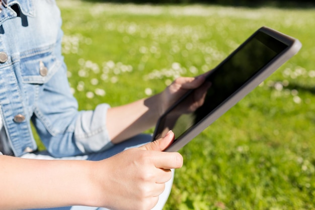 estilo de vida, verano, vacaciones, tecnología y concepto de personas - cerca de una joven con tablet pc sentada en el césped en el parque